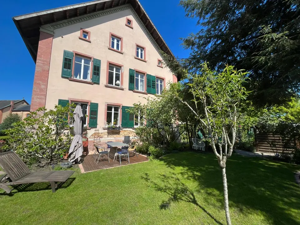 Das ehemalige Pfarrhaus in Unzhurst mit grünen Fensterläden und Garten im Sonnenlicht