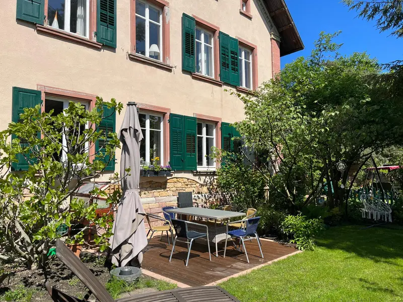 Terrasse mit Tisch und Sonnenschirm vor dem Pfarrhaus, Rasen und Bäume